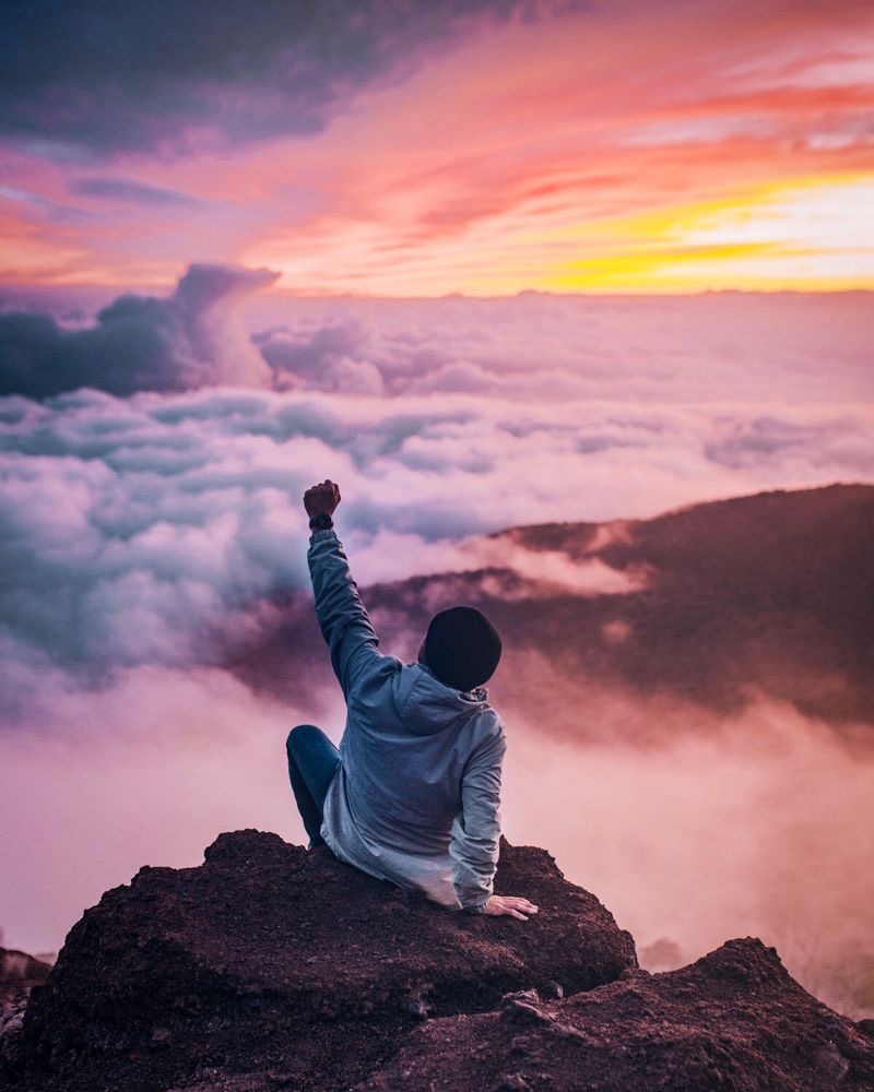 Un homme en haut d'une montagne au dessus des nuages fier d'avoir réussi cette ascension